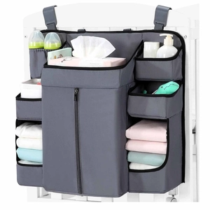 Detalle del organizador de cuna gris con grandes bolsillos para pañales y soporte para pañuelos
