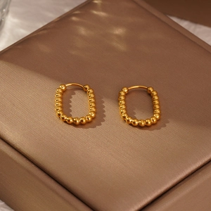 Détail de boucles d'oreilles créoles ovales dorées à perles sur un écrin en satin