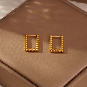 Détail de boucles d'oreilles rectangulaires perlées dorées sur un écrin à bijoux