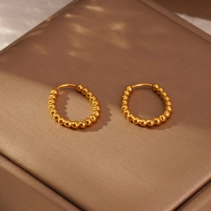 Détail de boucles d'oreilles créoles dorées à perles sur un coffret de présentation marron