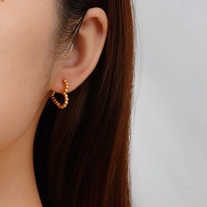 Gros plan de boucles d'oreilles cœur dorées perlées sur modèle avec texture élégante