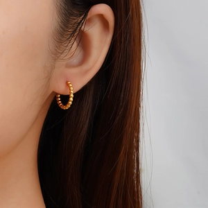 Gros plan d'une femme portant des boucles d'oreilles créoles dorées à billes style vintage