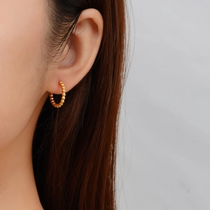 Gros plan d'un mannequin portant une boucle d'oreille créole perlée en or poli
