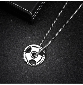 Close-up of silver barbell pendant with stainless steel chain on black textured surface