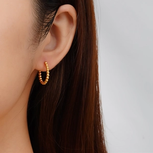Détail des boucles d'oreilles créoles dorées à billes avec design métallique texturé