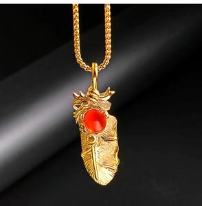 Vue macro détaillée du pendentif plume dorée serti d'une pierre précieuse rouge polie