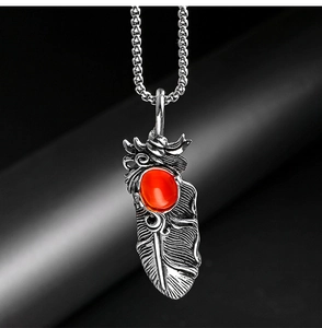Détail macro d'un pendentif plume en acier vintage avec pierre précieuse orange sertie