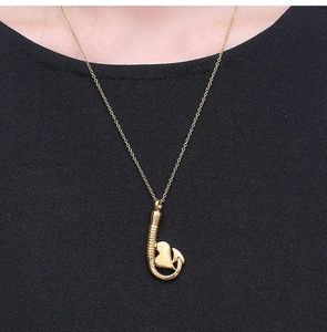 Primo piano di una collana con ciondolo a cuore dorato con dettaglio a amo da pesca