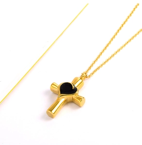 Dettaglio di una collana con pendente a croce dorata con intarsio a cuore nero e catena sottile