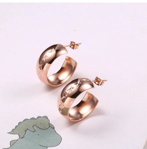 Close-up of rose gold C-shaped earrings with intricate star pattern engraving and stud back
