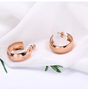 Close-up of rose gold stainless steel C-shaped earrings with diamond-pattern engraving