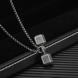 Vue macro d'un pendentif haltère avec texture en métal brossé mat sur boîte à bijoux noire