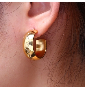 Macro detail of gold C-shaped hoop earrings with engraved cross patterns for women