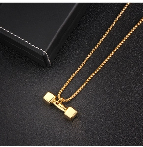 Détail d'un pendentif haltère doré avec une chaîne box polie sur une surface texturée noire