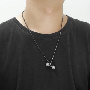 Détail du collier pendentif haltère en acier argenté vintage sur un t-shirt noir