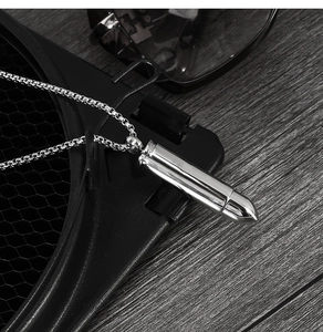 Pendentif en forme de balle en acier inoxydable poli présenté sur un support texturé noir