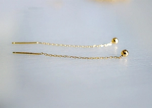 Détail de longues boucles d'oreilles traversantes en or 18K avec perles sur marbre
