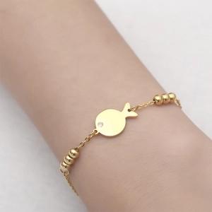 Detail of a gold fish bracelet with tiny zircon eye on a minimalist stainless steel chain