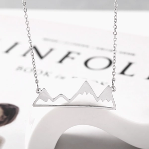 Detailed macro view of a silver mountain peak pendant on a fine chain over a magazine