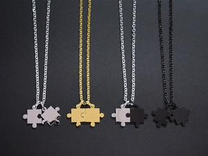 Detail von Puzzleteil-Halsketten in Gold, Silber und Schwarz auf mattem Hintergrund