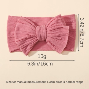 Pink elastic infant headband with large ribbed knit bow on a warm yellow background