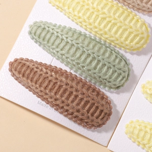Close-up of three knitted teardrop hair clips in yellow, green and brown on a card