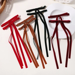 Close-up of velvet bow hair clips in deep red, brown, and green with long ribbon streamers