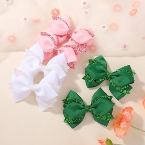 Close-up of pink, white, and green glitter bow hair clips set on a floral aesthetic background