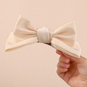 Detail showing creamy white satin fabric texture and metal clip of the bow hair accessory