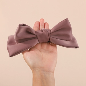 Close-up of a large dusty pink satin bow hair clip held by hand for scale and texture