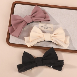 Three bow hair clips in rose, cream, and black displayed on a linen texture tray