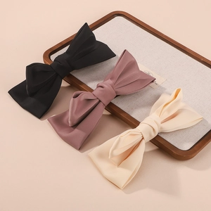 Three elegant satin bow hair clips in black, dusty rose, and beige on a wooden tray