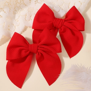 Detail view of two vibrant red bow hair clips with textured waffle fabric on white lace