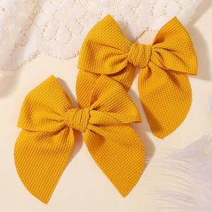 Detail of mustard yellow waffle texture bow hair clips for kids on lace background