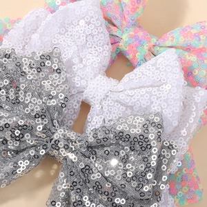 Close-up of glitter bow hair clips in white, silver, and iridescent pink for girls