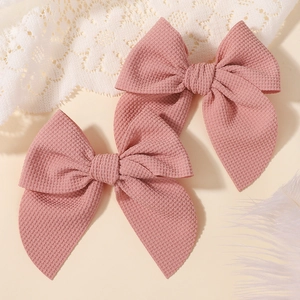 Detail of two dusty pink bow hair clips featuring soft waffle textured fabric on beige lace