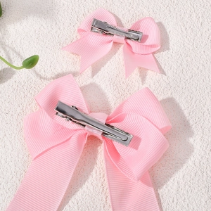 Close-up of pink grosgrain ribbon hair bows with silver metal clips on a textured surface