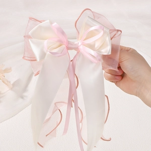 Detailed close-up of layered cream satin and pink chiffon bow hairpin with wavy edges