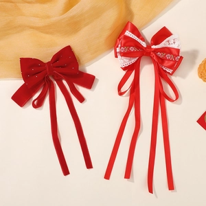 Détail de barrettes à nœuds en velours et satin rouge avec longs pompons et dentelle