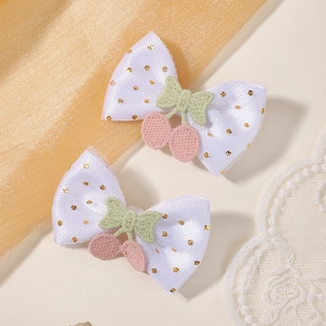 Détail de pinces à cheveux en maille blanche avec pois dorés et broderie cerise