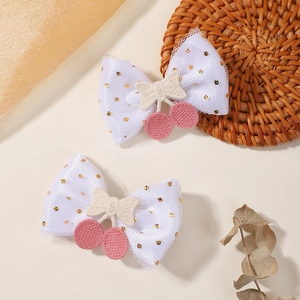 Détail de pinces à cheveux en maille blanche avec cerises brodées et pois dorés