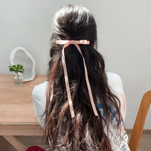 Pink ribbon bow hair clip with long tassels worn on dark wavy hair for women and girls