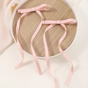 Detail view of two soft pink ribbon bow hair clips with long tassels on a wooden tray