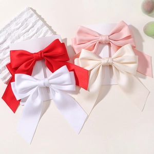 Dettaglio di quattro fermagli per capelli in raso rosso, bianco, rosa e beige su carta
