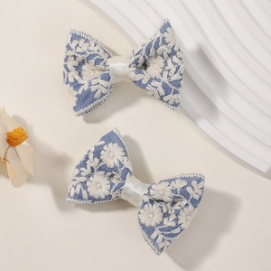 Detail van blauwe haarspelden met witte geborduurde bloemen voor meisjeskapsels