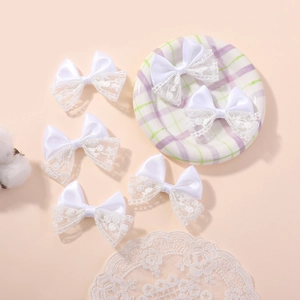 Detailed view of six white lace and satin bow hair clips on a vintage decorative plate