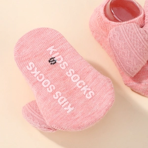 Detail of pink knitted baby sock with white non-slip KIDS SOCKS lettering on the sole