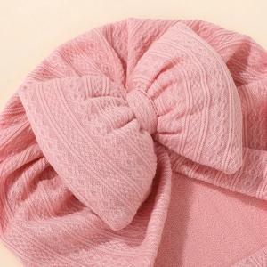 Close-up of pink knit baby turban hat featuring a large bow and ribbed texture detail