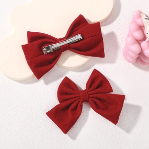 Detailed view of red velvet bow hair clips with silver metal duckbill clip on white board