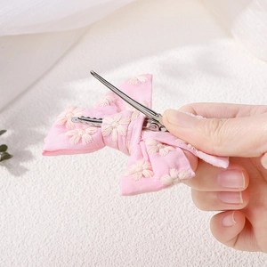 Detailed close-up of pink fabric hair clip with white floral embroidery and silver metal base